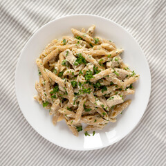Homemade Chicken Alfredo Penne with Parsley on a white plate, top view. Overhead, from above, flat lay.