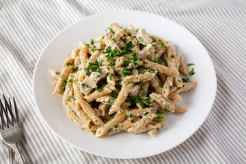 Homemade Chicken Alfredo Penne with Parsley on a white plate, low angle view.