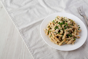 Homemade Chicken Alfredo Penne with Parsley on a white plate, side view. Copy space.