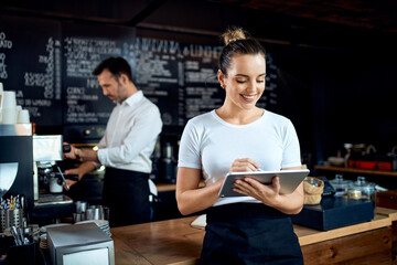 Successful small business owner standing with digital tablet in a cafe