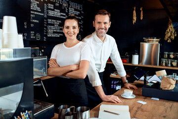 Two small business owners standing together in cafe smiling at camera