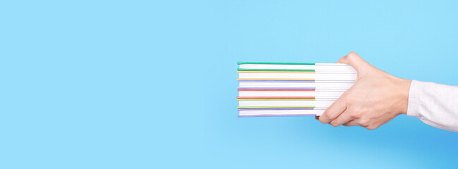 Hand with stack of books on blue background.