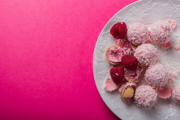 exquisite coconut candies lie on a white plate studded with raspberries on a bright pink colorful background. High quality photo