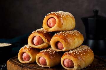 Homemade sausages in dough (pigs in blanket) on a wooden board, dark background