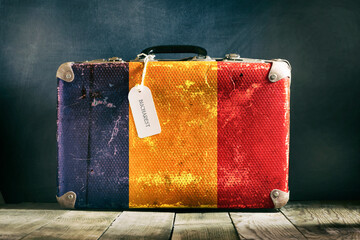 Old suitcase with the Romania flag on wooden background.