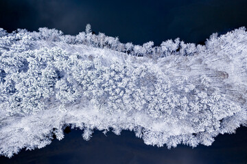 Flying above cold river and snowy forest in winter