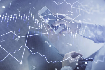 Double exposure of man's hands holding and using a digital device and forex graph drawing. Financial market concept.