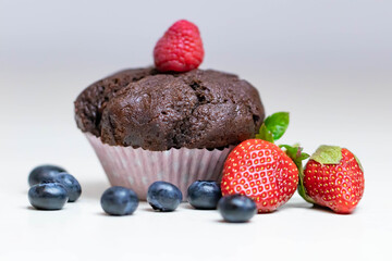 Baked chocolate muffin with juicy berries, strawberries, blueberries, raspberries.