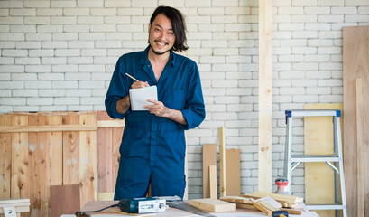 Good looking Asian carpenter wearing coverall dress working for DIY jobs in carpenter room with...