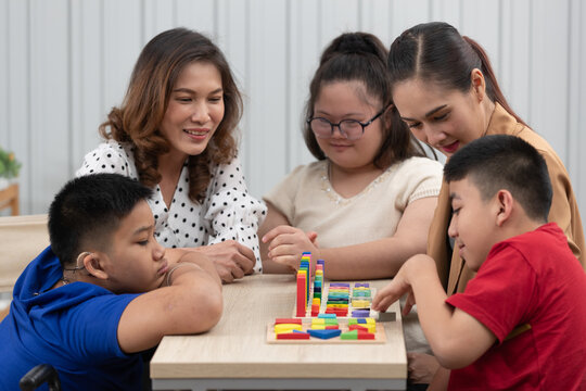 Group of special students in classroom, a down syndrome girl, two handicapped boys and cute Asian teacher playing toy and game together