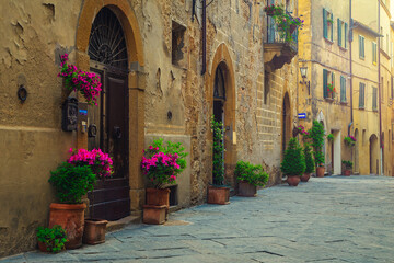 Fototapeta na wymiar Cozy street and entrances decorated with colorful flowers, Pienza, Italy