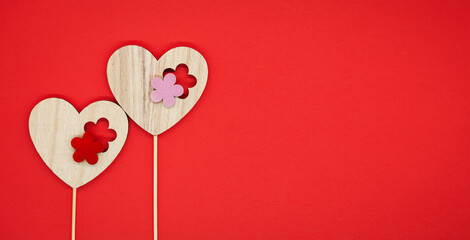 Festive background. Concept for valentine's day, love, wedding. Red background. Two decorative wooden hearts on sticks. Free space for text on the right.