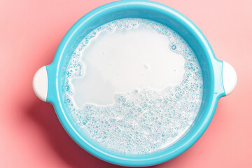 Blue basin with soapy water on pink background top view.