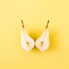 Fresh pear cut in half on a yellow paper background. Summer fruit creative concept. Flat lay arrangement.