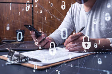 A businessman in casual wear signing the contract to prevent probability of risks in cyber security. Checking the phone. Padlock Hologram icons over the working desk.