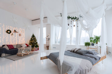 large very bright spacious stylish open plan Bali style apartment with hanging bed and panoramic windows. white floor and walls, simple wooden furniture. decorated with a christmas tree