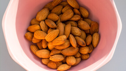 brown almonds lie in a pink plate in the sun