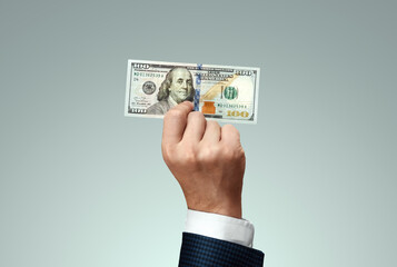 Businessman's hand holding a hundred dollar bill. The concept of salary, investment, donation.