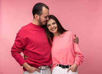 Photo of sweet couple hug each other and smile. Male and female are in love, isolated over pink background