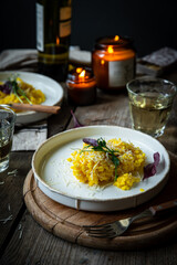 Rustic dinner with risotto all Milanese< wine and candles. Risotto with Saffron and parmesan on white plate on wooden table. 