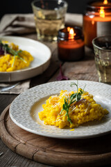 Rustic dinner with risotto all Milanese< wine and candles. Risotto with Saffron and parmesan on white plate on wooden table. 