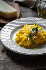 Rustic dinner with risotto all Milanese. Risotto with Saffron and parmesan on white plate on wooden table. 