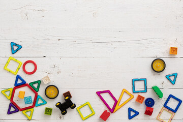 Close up of plastic multicolored constructor. Top view of children's educational toys, magnetic figures, colorful cubes, bricks on a white wooden background.