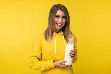 Photo of attractive lady holds bootle of milk, feels nice about dairy products. Wears casual yellow hoody, isolated yellow color background