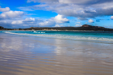 Pattern in sand leading to rocky coastline and cloudy sky 