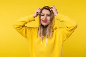 Photo of attractive lady in the hood poses in a cute way. Wears casual yellow hoody, isolated yellow color background