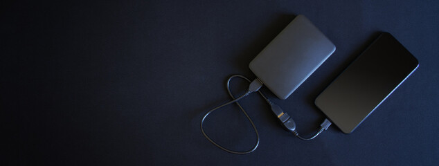 A smartphone and an external hard drive connected to it with an OTG cable lie on a black...