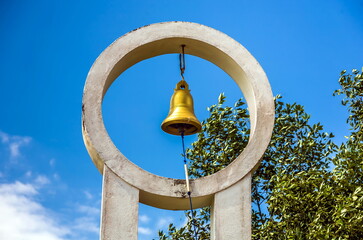 Bell on the pedestal of a religious building in Sri Lanka against the background of foliage of trees and blue sky with white clouds