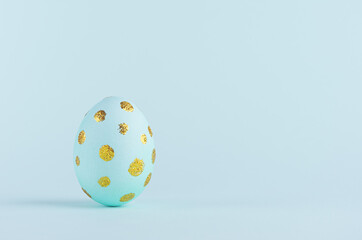 Blue easter egg with gold glitter dots standing on blue background, copy space.