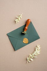 Green paper envelope with wax seal stamp and dried leaves on pastel beige background. Flat lay, top view. Romantic letter concept.