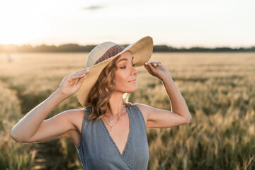 Girl in a wide-brimmed hat on a wheat field in the rays of the setting sun