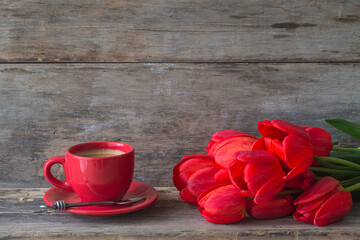 Holiday's greeting card. Red cup of coffee and bunch of red tulips on old non paint wooden background. Space for text