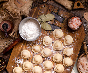 homemade dumplings with meat on rustic wooden board and table with flour, sackcloth