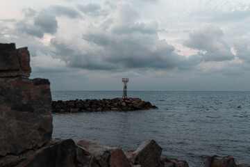 Fototapeta na wymiar small rusty lighthouse dark clouds scenery seen through rocks winter time greece