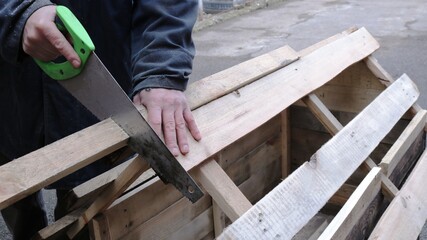 sawing off a part of the board during the construction of a roof for a doghouse using a hacksaw in the hands of a carpenter, making a wooden product in the countryside
