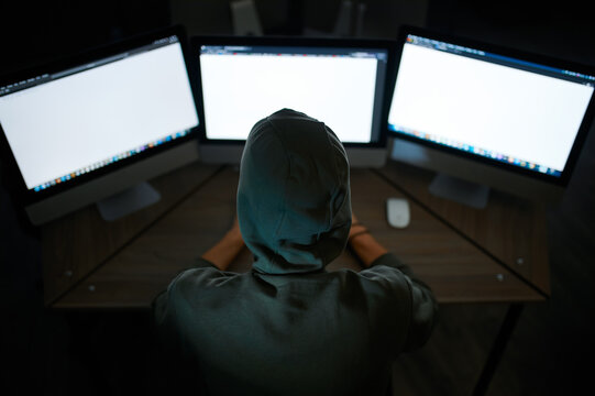 Male internet hacker in hood sitting at monitors