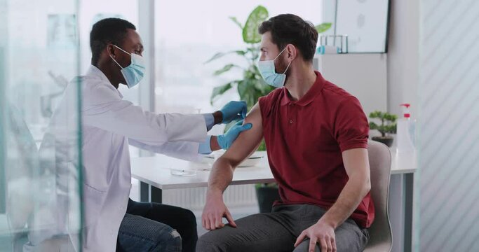 Young caucasian male patient visiting doctor for vaccoination process. Doctor pharmacist analyzing young man injecting vaccine against coronavirus.