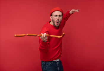 Photo of happy man with beard in glasses and red clothing. Plays sausages like nunchucks ninja,...