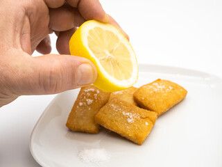 Hand squeezing a lemon on fresh panelle. Traditional Sicilian panelle on dish. Typical Sicilian street food. White Background.