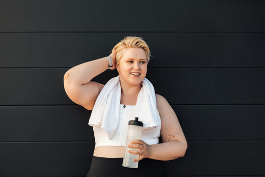 Smiling plus size woman standing at wall. Positive woman relaxing after training and adjusting hair.