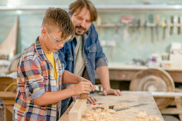 Father teaches his young son to plan wood in a carpentry workshop. Empty space for text