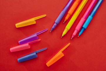 Colorful pens with caps closeup, red background