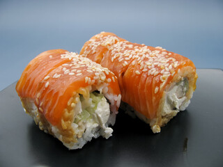 Philadelphia sushi with cheese and cucumbers on a black plate on a blue background.