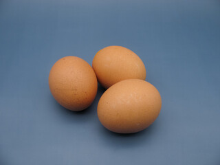 three brown raw chicken eggs on a blue background