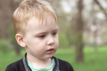 Close up portrait of cute &ETH;&iexcl;aucasian baby boy on green park background. Blue eyes, blond hair, looking to right side of shot. Spring time, outdoors, copy space.
