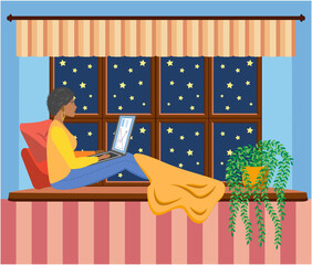A woman works at a laptop while sitting on the windowsill at home. Freelance concept, quarantine due to covid-19.